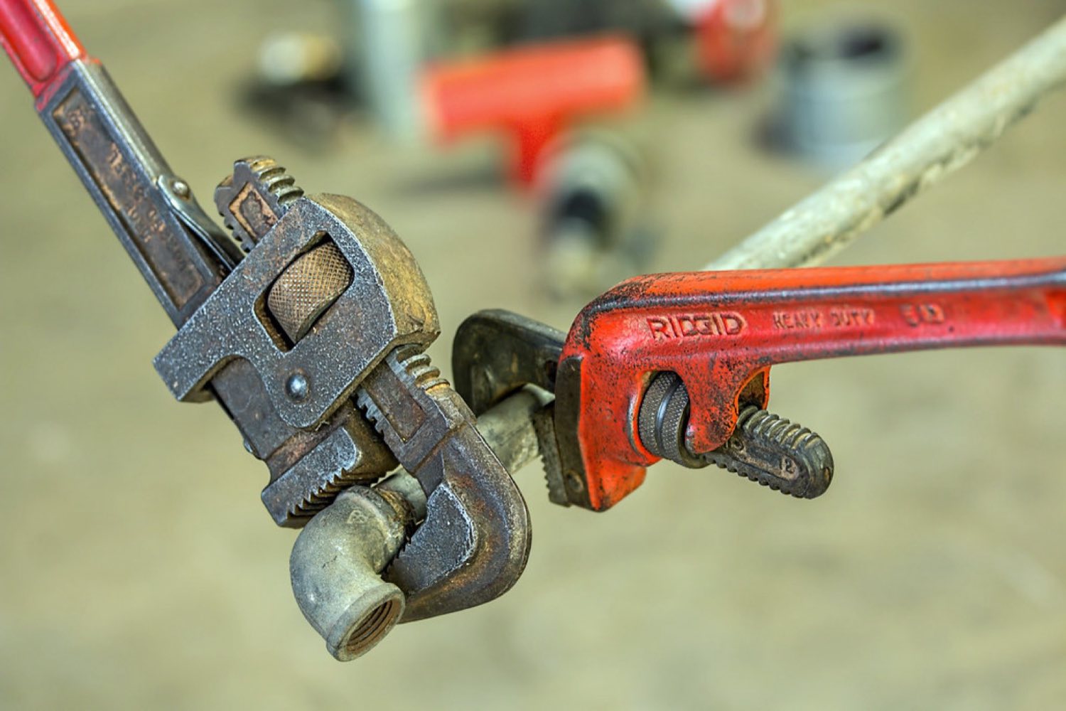 Close-up of a Reliable Home Solutions plumber's pipe wrenches gripping a fitting